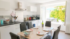 A modern kitchen with white cabinets, a dining table set for four, and a view of the outdoors. - Holidays for 6 in Saint Guénolé (Penmarch)