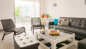 A modern living room with a sofa, two chairs, a coffee table with a chess set, and a bookshelf with toys. - Holidays for 6 in Saint Guénolé (Penmarch)