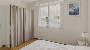 Ett hotellrum med en säng, ett fönster med tunna gardiner, en tavla på väggen och ett nattduksbord med en lampa.