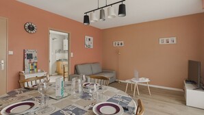 En matplats med ett bord dukat för fyra personer, en soffa, en tv och ett kök i bakgrunden.
