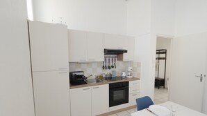 Una cucina moderna con mobili bianchi, un forno nero e un'area pranzo con tavolo bianco e sedia blu.