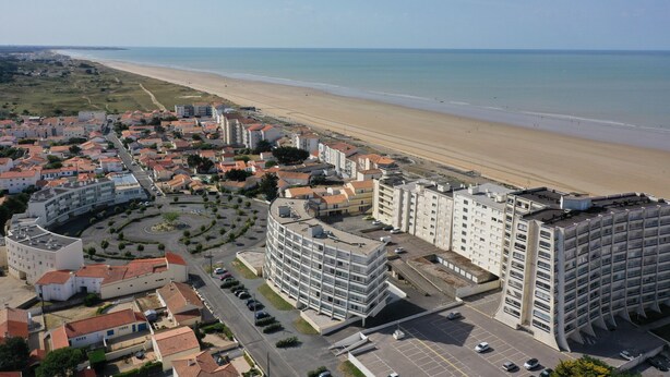 Una località balneare con spiaggia, edifici moderni e un parcheggio.