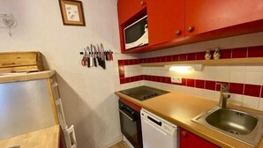 Uma cozinha compacta com armários vermelhos, micro-ondas, pia e lava-louças.