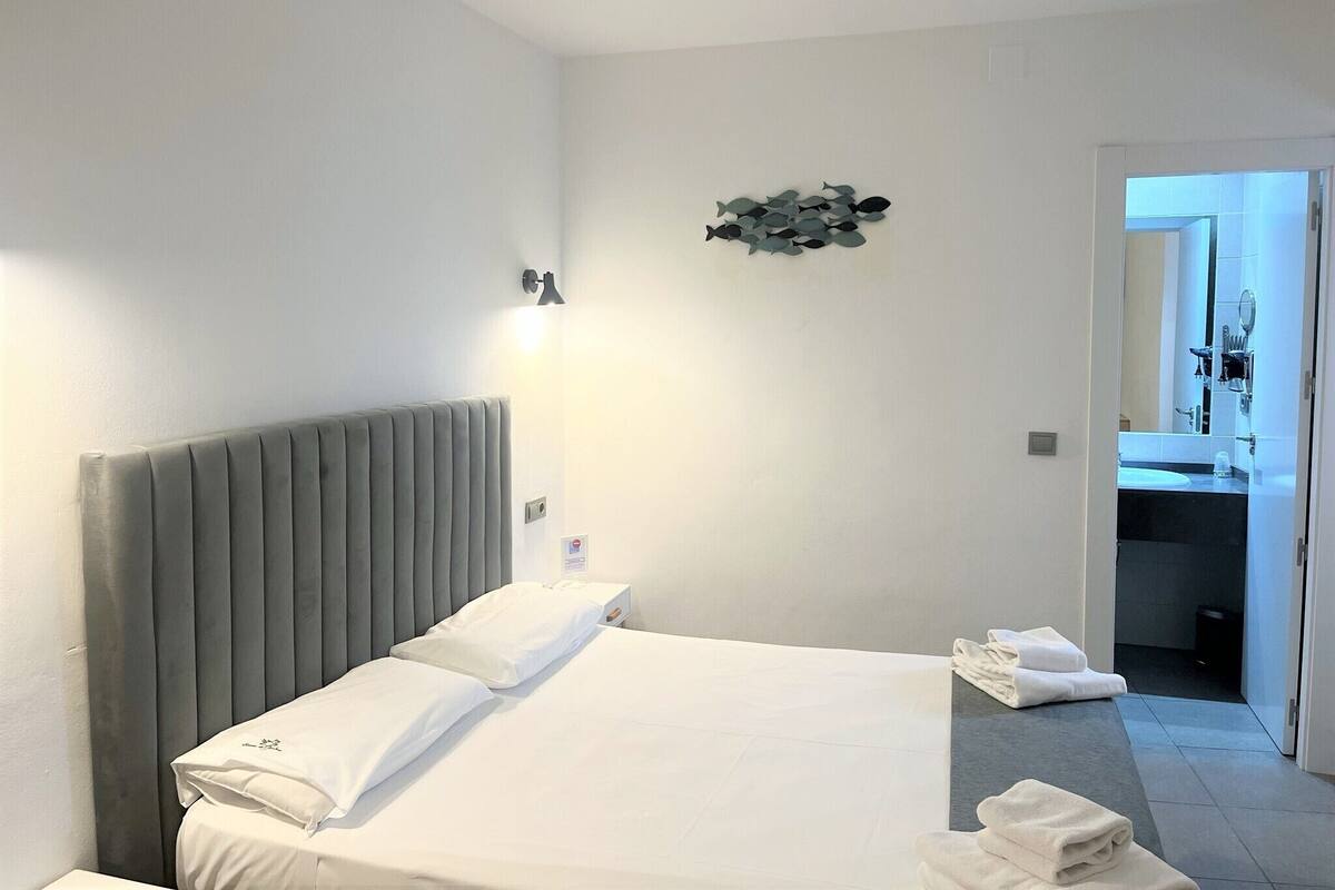 Habitación de hotel con cama, lámpara de pared y baño visible a través de una puerta abierta.