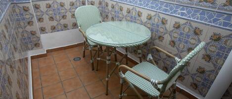 Un pequeño patio con una mesa redonda y dos sillas de mimbre, rodeado de paredes decorativas con azulejos.