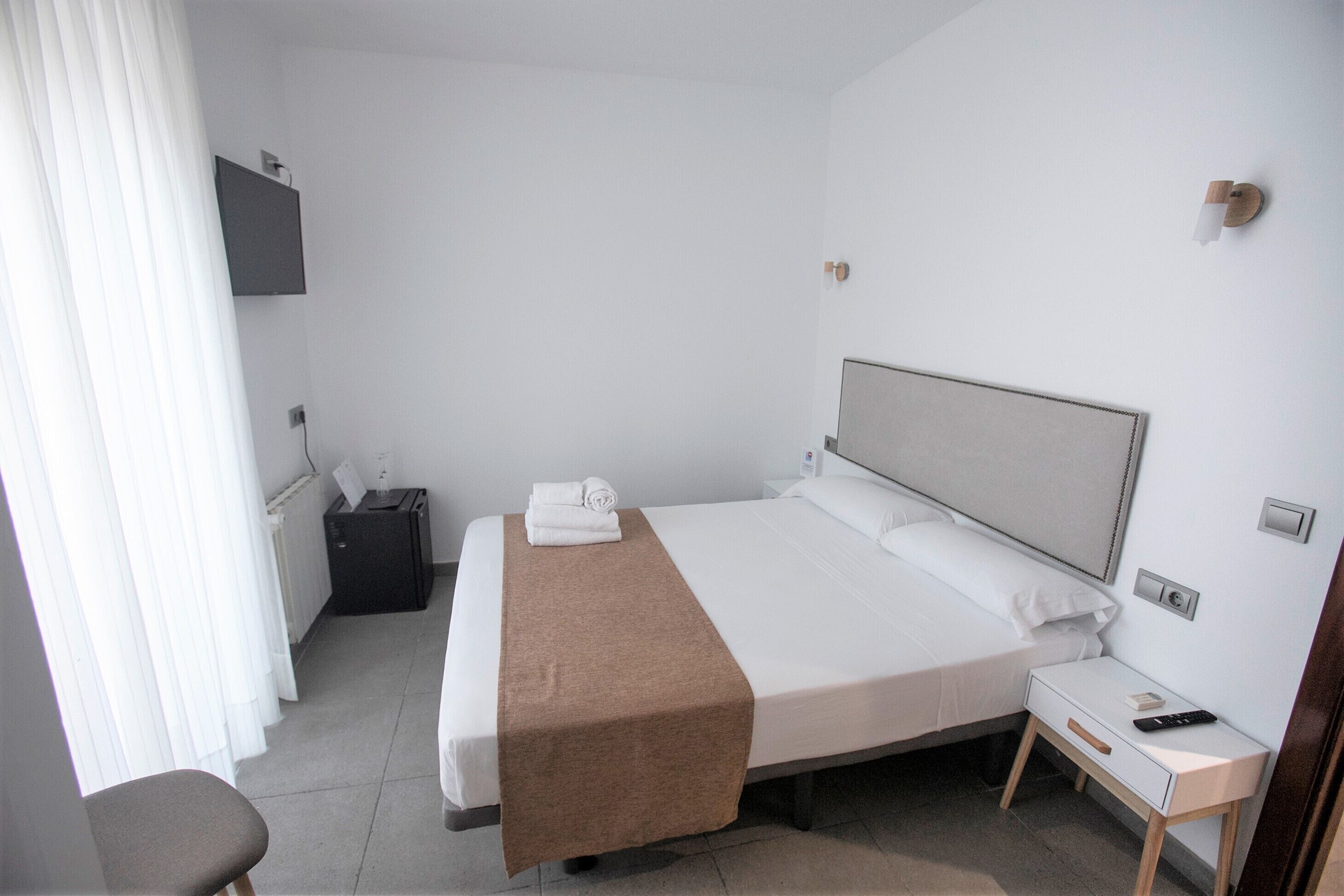 A hotel room with a bed, bedside table, and a TV mounted on the wall.