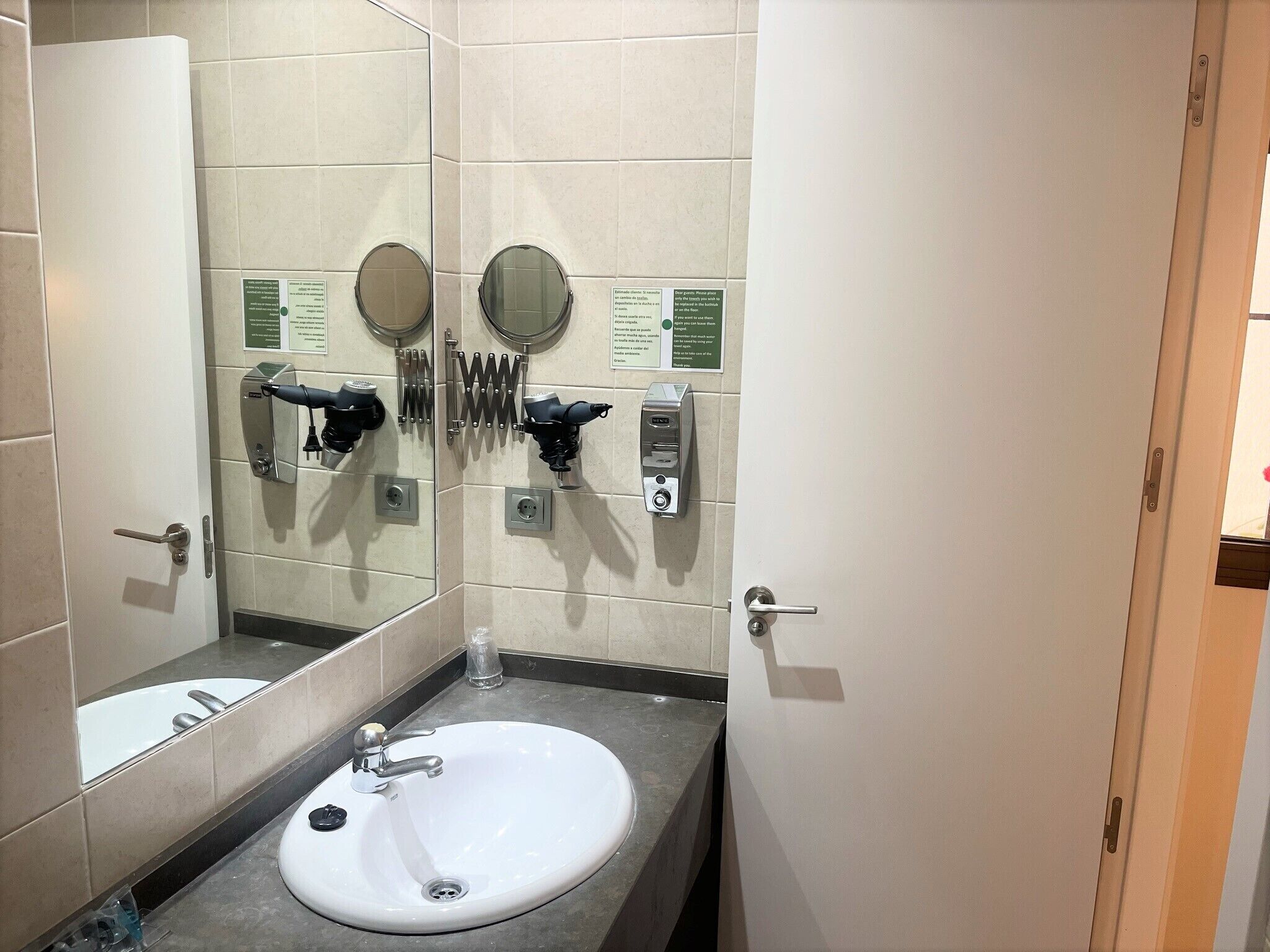Une salle de bain avec un lavabo blanc, deux miroirs et un distributeur de serviettes.
