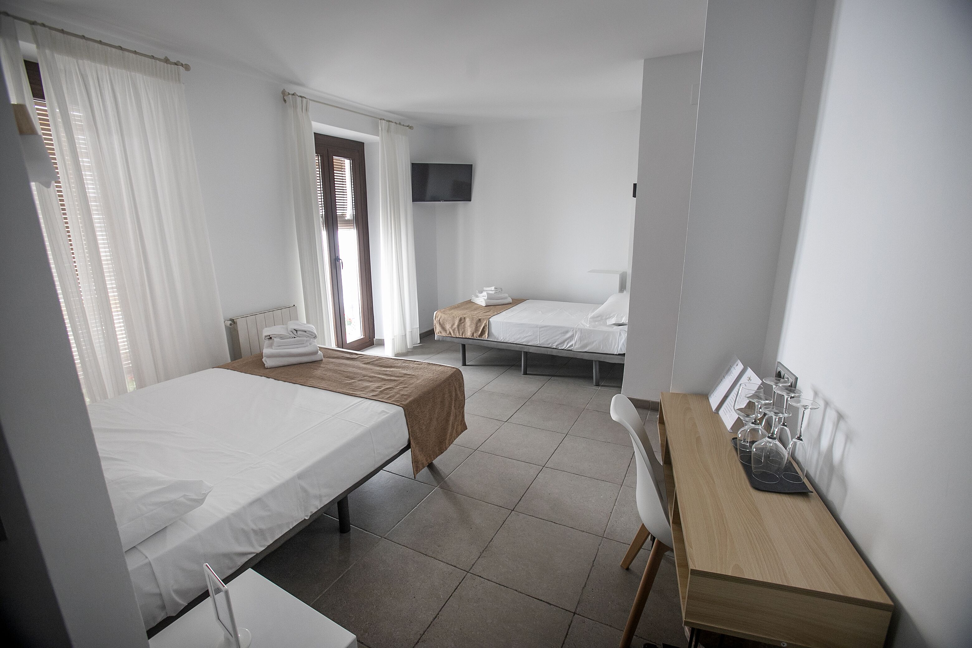 Habitación de hotel con dos camas, un escritorio, un televisor y una ventana con cortinas.