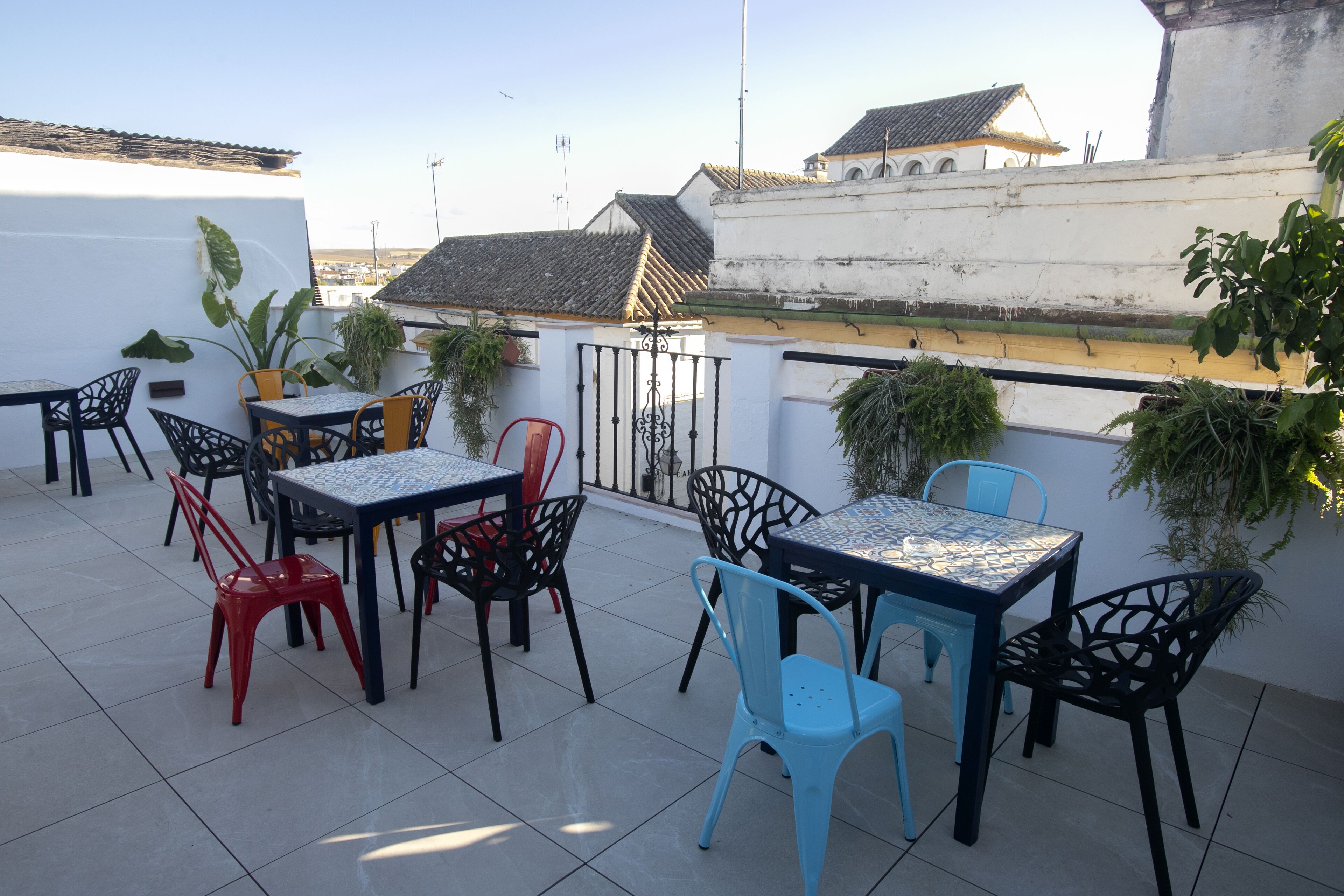 An outdoor patio with tables and chairs, potted plants, and a view of buildings in the background.