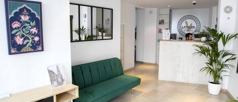 A reception area with a green sofa, a wooden console table with a framed picture, a potted plant, and a reception desk with a circular logo.