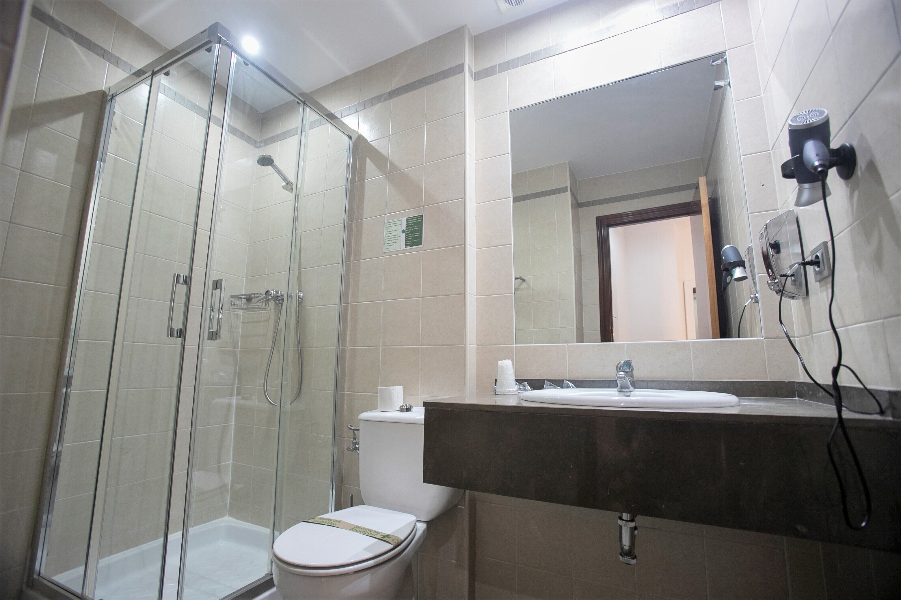 Un baño con ducha de vidrio, inodoro y lavamanos con espejo arriba.