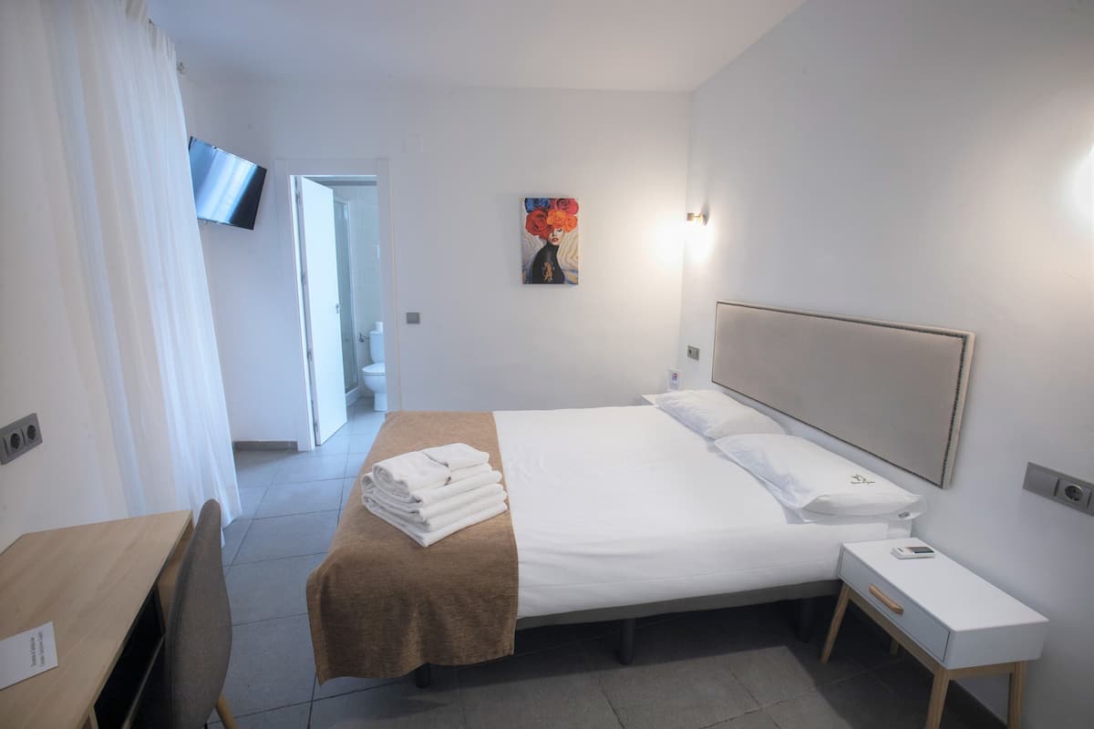 Habitación de hotel con cama, mesita de noche, televisor montado en la pared y un cuadro.