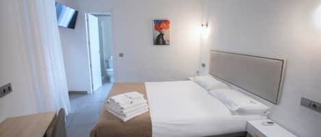 A hotel room with a bed, a bedside table, a TV mounted on the wall, and a painting on the wall.