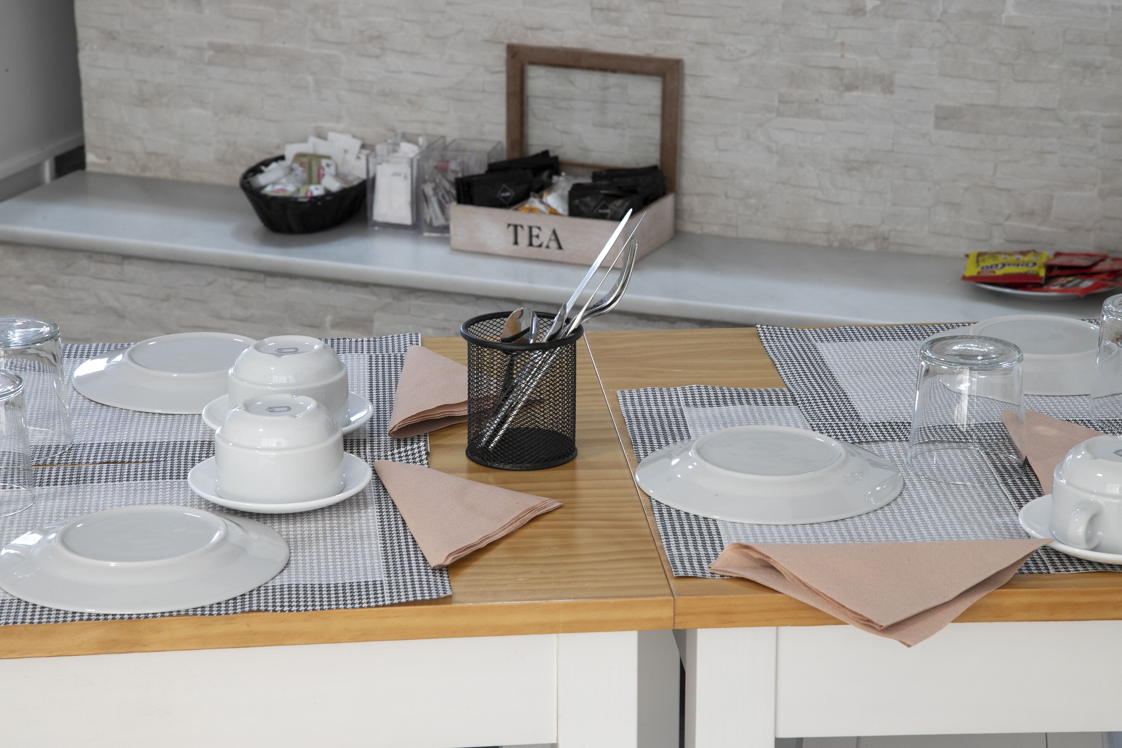 A neatly arranged dining table with white plates, bowls, and a tea box labeled "TEA" in the background.