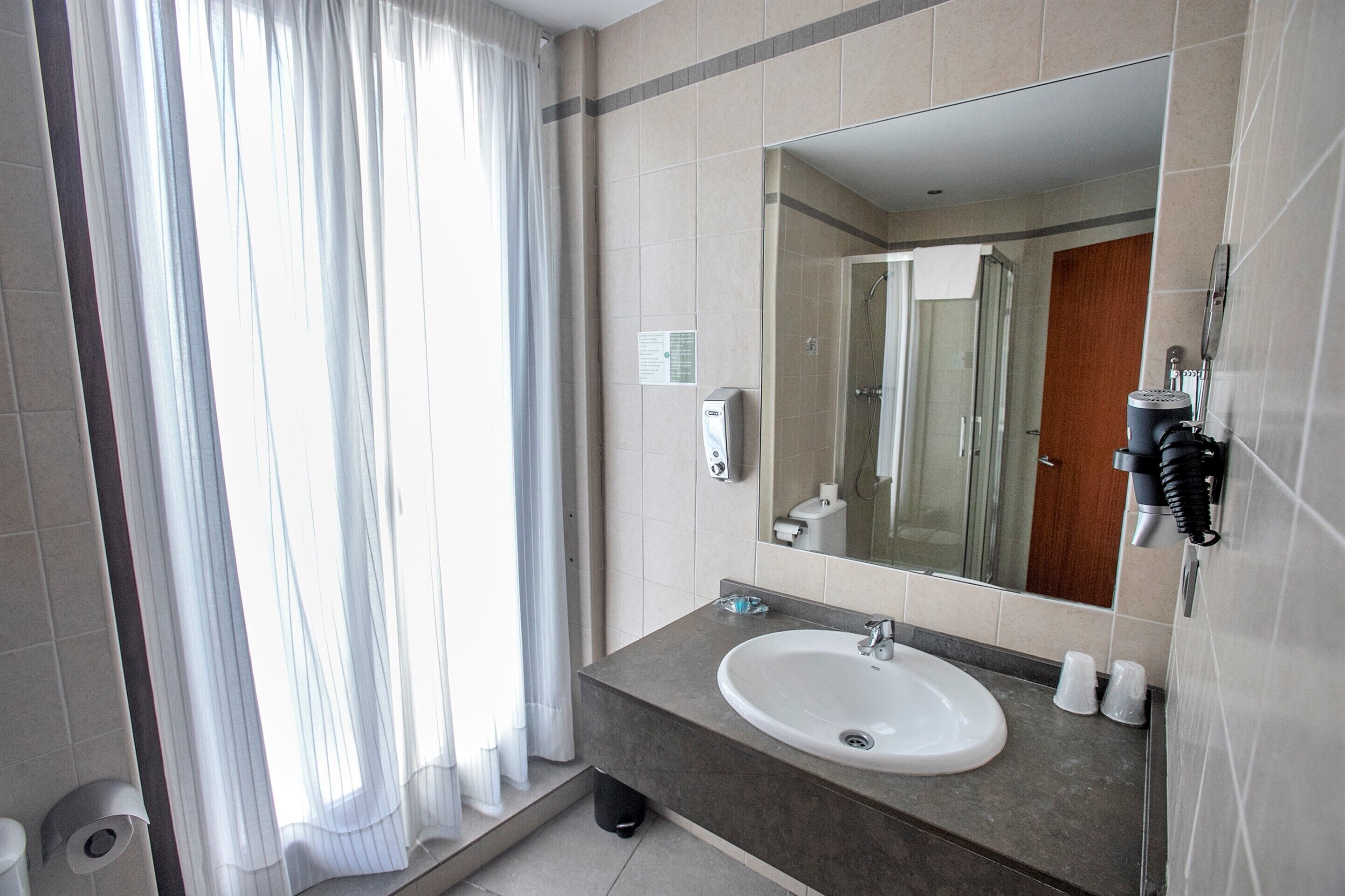 A modern bathroom with a large mirror, a sink, and a shower area.