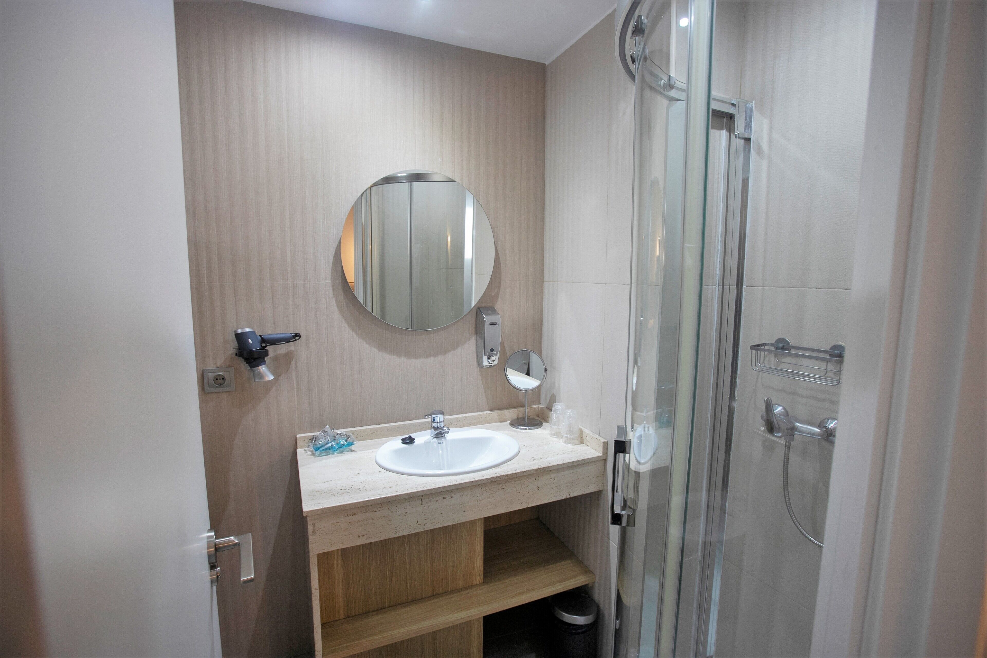 Een moderne badkamer met een houten wastafelmeubel, een ronde spiegel, een douchecabine met glazen wanden en een handdoekrek.