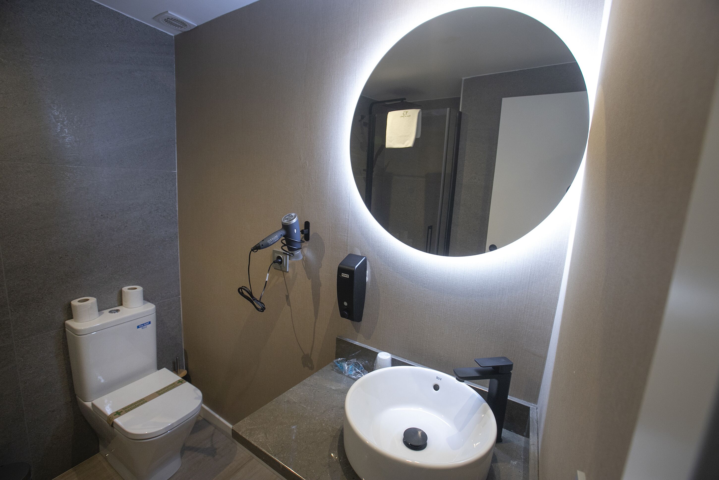 Une salle de bain équipée de toilettes, d’un lavabo, d’un miroir et d’un sèche-mains.