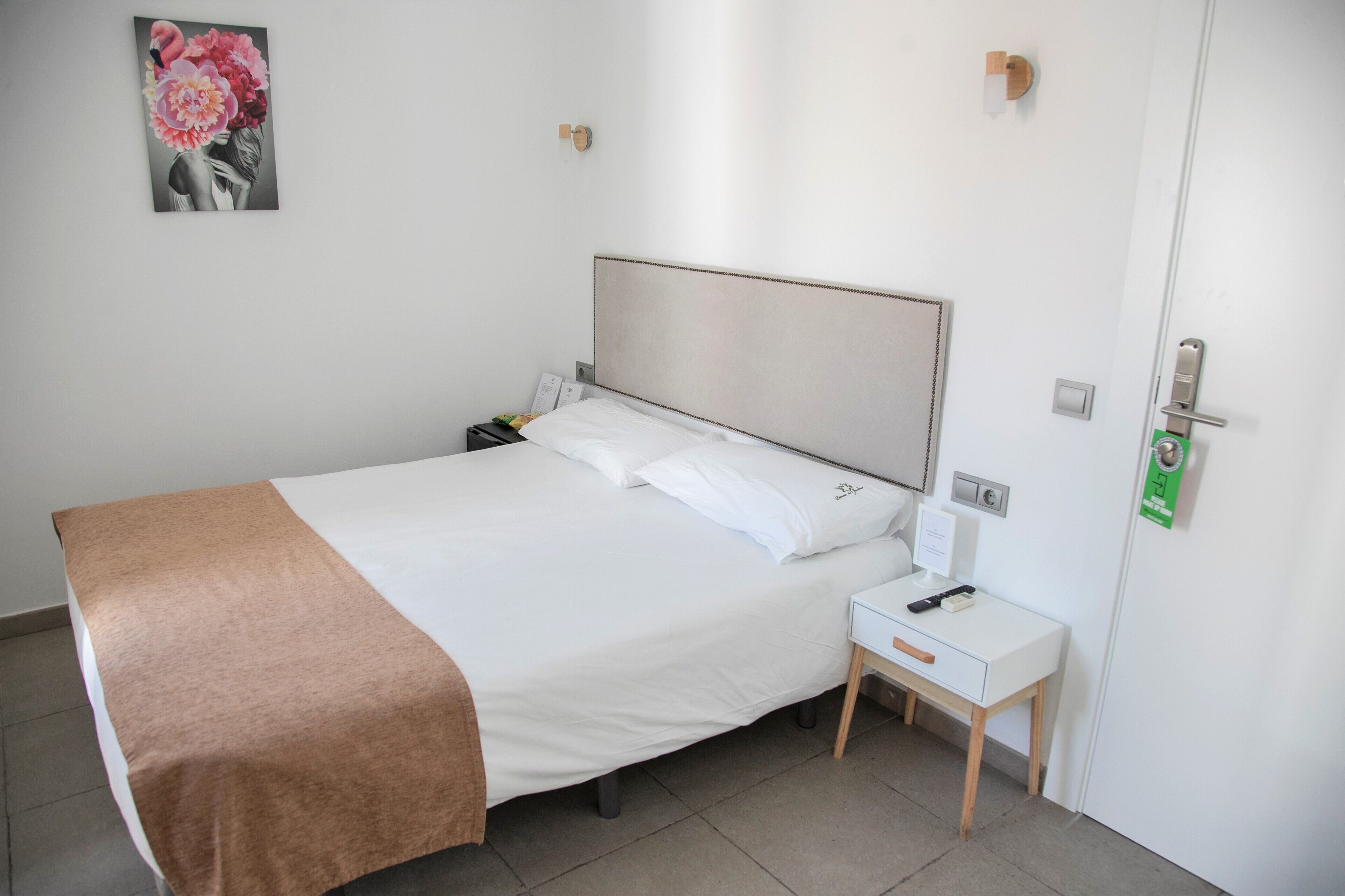 A neatly made bed with a white and brown bedspread, a bedside table with a lamp, and a wall-mounted light fixture.