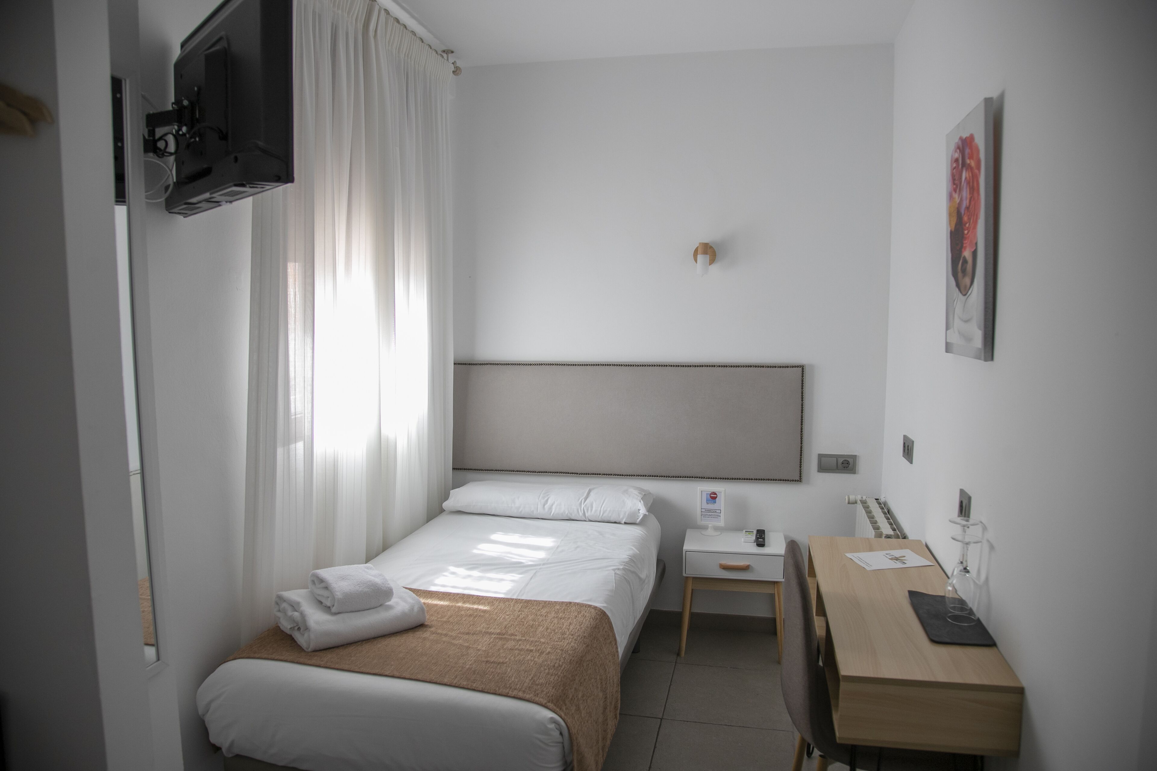 Een hotelkamer met een bed, bureau, stoel, tv aan de muur en een raam met gordijnen.