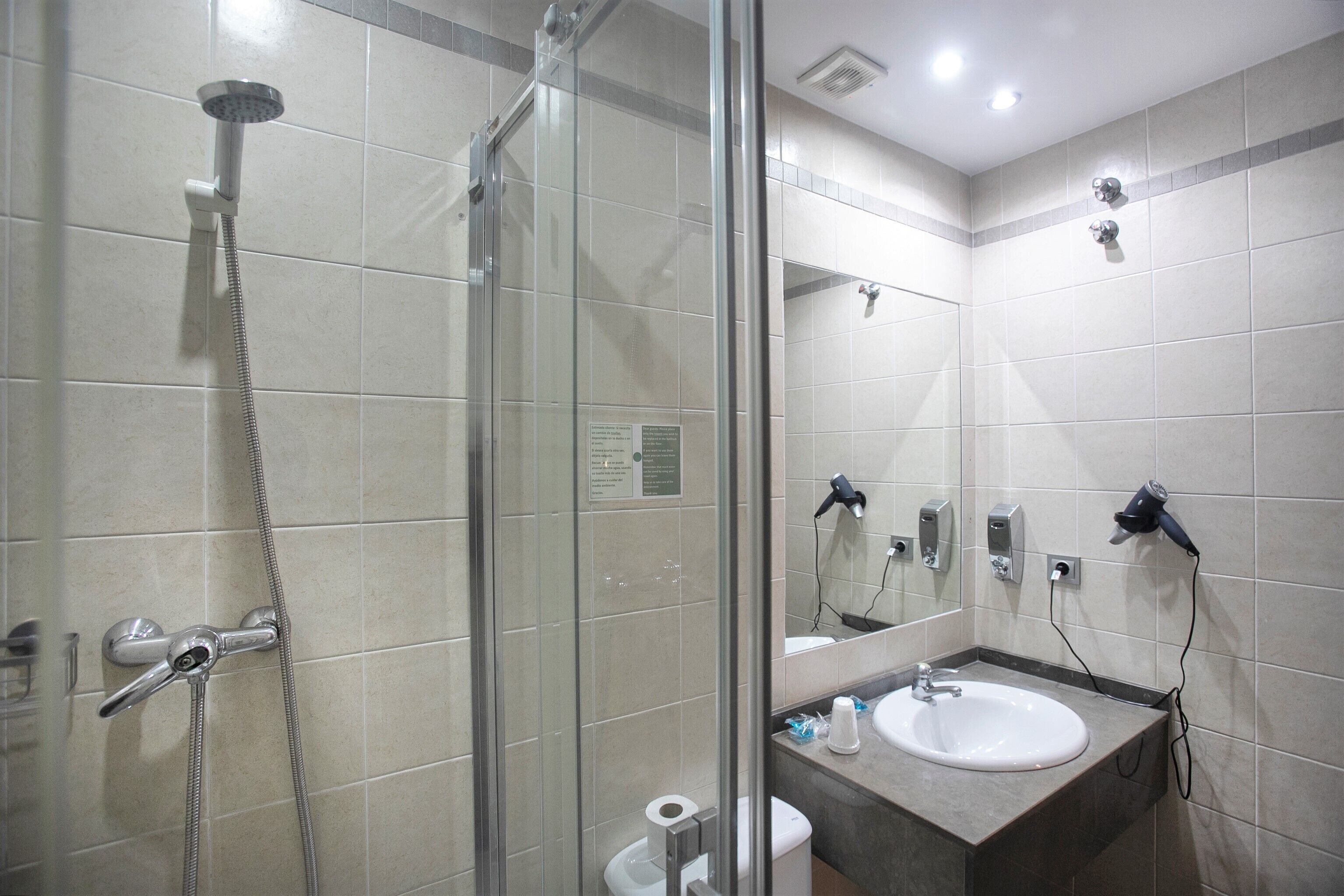 Ein modernes Badezimmer mit einer in Glas abgeschirmten Dusche, einem Waschbecken und einem Spiegel.