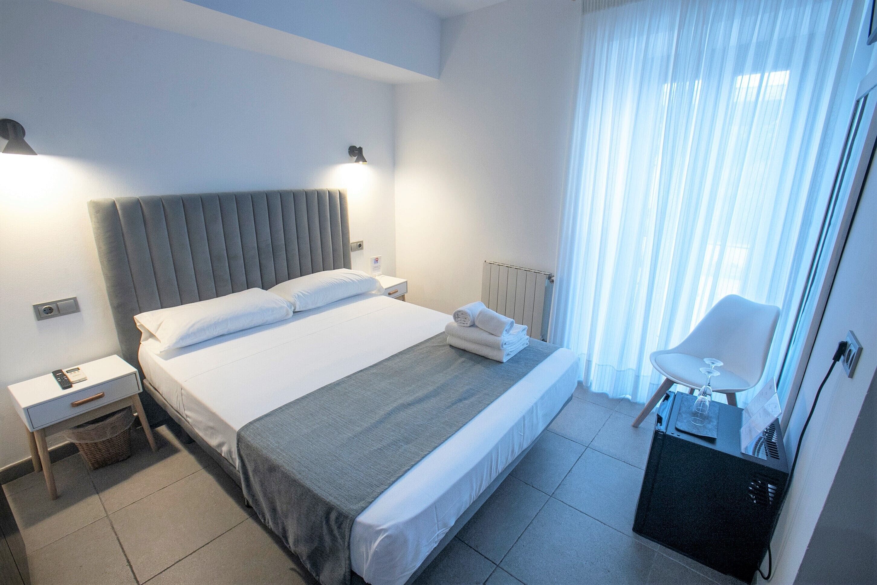 A hotel room with a bed, bedside tables, a chair, and a radiator.