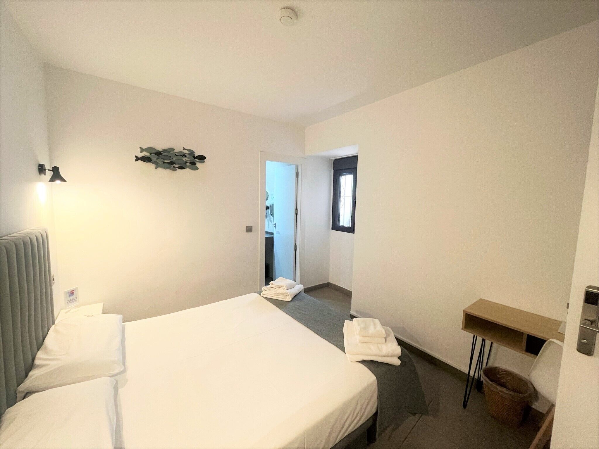 Habitación de hotel con una cama grande, un escritorio, una silla, un radiador y un ventanal pequeño.