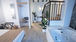 Una habitación de hotel moderna con una bañera grande, un escritorio, una silla y una planta en maceta.