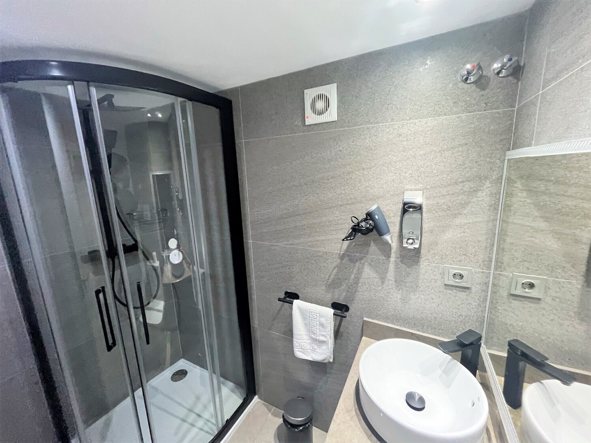 A modern bathroom with a glass-enclosed shower, a large sink, and a mirror.