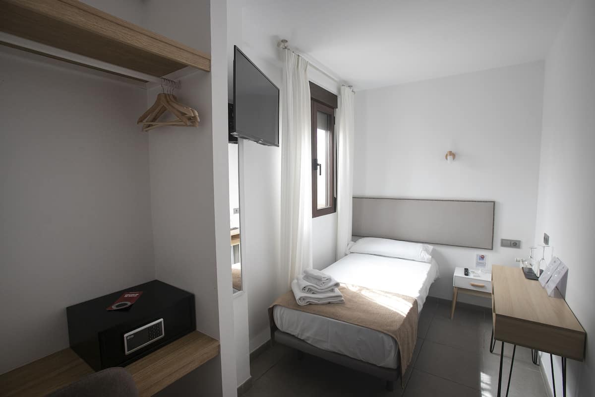 Habitación de hotel con cama, mesita de noche, escritorio, televisor montado en la pared y estante de madera.