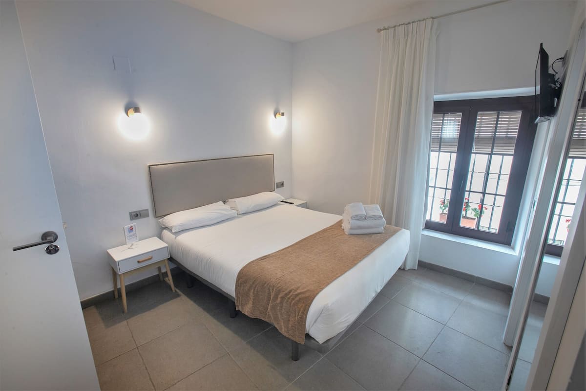 Una habitación de hotel con cama, mesitas de noche, una ventana con cortinas y una puerta.