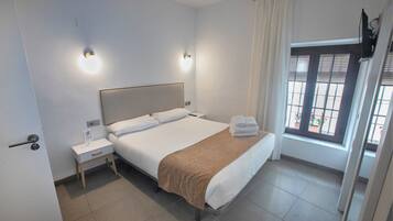 A hotel room with a bed, bedside tables, a window with curtains, and a door.