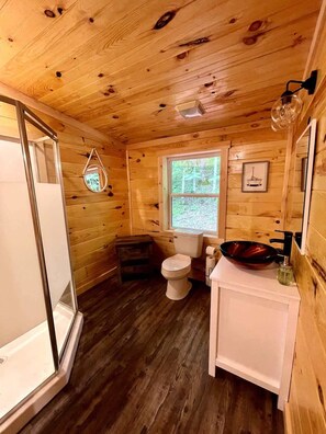 A wooden cabin bathroom with a toilet, sink, and a small window.