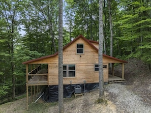 A wooden cabin with a porch and a small deck, surrounded by trees.