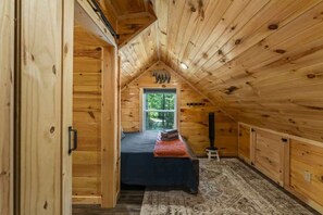 A cozy attic bedroom with a sloped ceiling, a bed, a window, and a small stool.