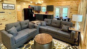 Interior d'una cabana acollidora amb sostre de fusta, un sofà modular, una taula de centre rodona i una escala que condueix a un nivell superior.