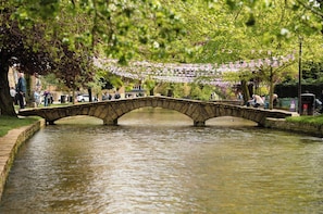 A stone bridge over a calm river, surrounded by trees and a festive string of flags.