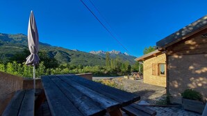 Ein Holztisch für ein Picknick mit Sonnenschirm, ein kleines Holzgebäude und eine gebirgige Landschaft im Hintergrund.