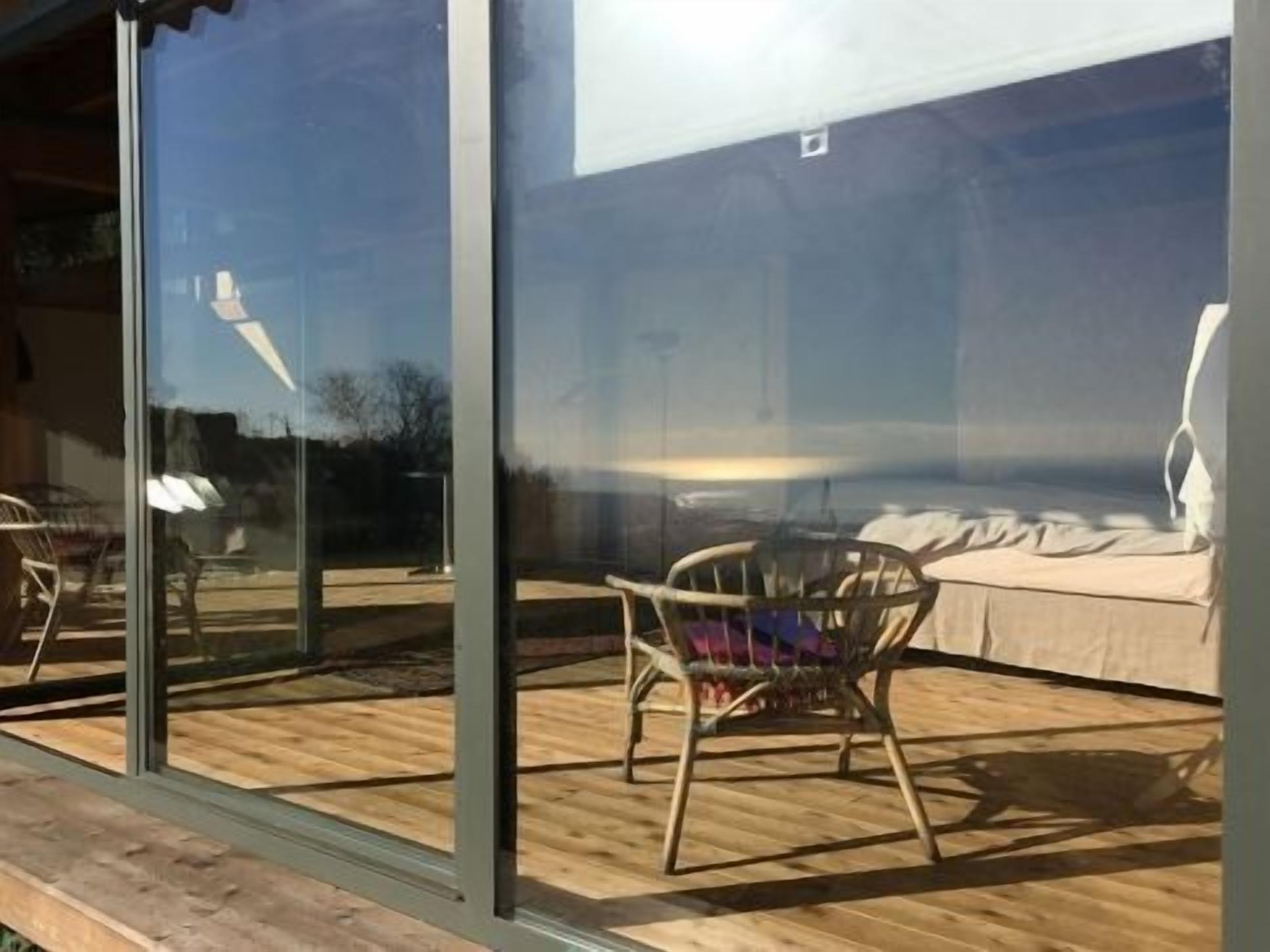 A room with a large window, a wooden deck, and a bed with a white cover.
