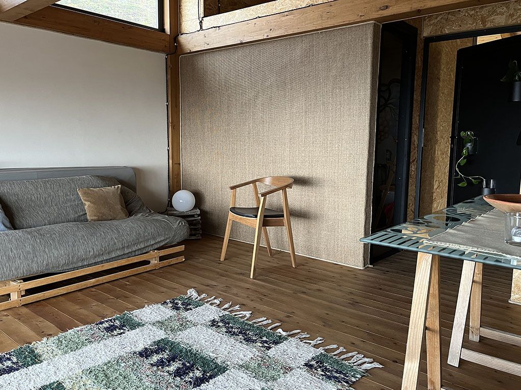 Un salon chaleureux avec un canapé gris, une chaise en bois, une table en verre et un tapis à motifs.