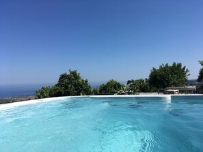 Una piscina infinita de agua cristalina con vistas al océano y un horizonte urbano distante.