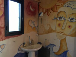 Un baño con lavamanos, espejo y un mural en la pared.