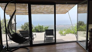 Een kamer met een grote schuifdeur naar een terras buiten, met twee stoelen en een hangstoel.