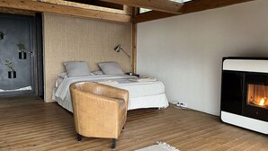 Een moderne slaapkamer met een bed, een stoel, een open haard en uitzicht op het landschap.