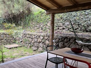 Un patio cubierto con una mesa, sillas, una hamaca y un muro de piedra al fondo.