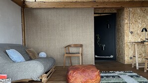 Een gezellige kamer met een bank, een houten stoel, een leren poef en een kamerbreed tapijt met dessin.