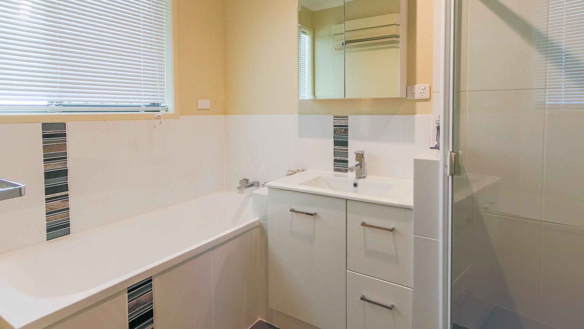Ein kleines, modernes Badezimmer mit einem weißen Waschbecken, einem Spiegel und einer Duschkabine.