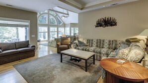 Een ruime woonkamer met een hoge plafond, grote ramen en een gezellige zithoek met een gestreept sofa en een leren fauteuil.