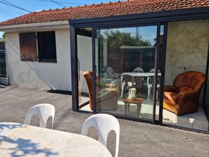 Et hus med tegltag og en skydedør, der fører til en udendørs terrasse med et bord, stole og en sofa.