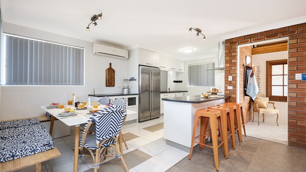 Een moderne keuken met een centraal eiland, witte kasten en een accentmuur van baksteen.