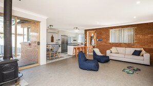 Een woonkamer met een bank, blauwe loungestoelen, een open haard en een keuken op de achtergrond.